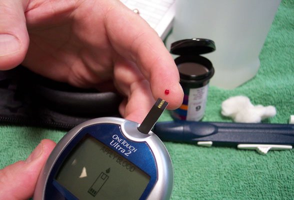 han hovering over glucose reader with pin prick of blood on index finger for blood sugar testing
