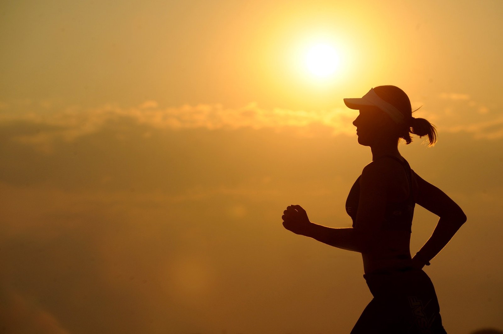 Silhouette of a woman with a ponytail wearing a sun visor, running against the backdrop of the midday sun